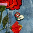 Ręcznie malowana przypinka w kształcie serca w środku retro czaszka z kwiatem wpięta w jeansową kurtkę od producenta ręcznie malowanych pinów od Pinswear