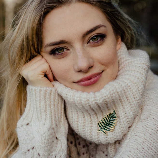 Piny na zamówienie Paproć z serii las wpięty w golf kremowego swetra piegowatej młodej dziewczyny od producenta ręcznie emaliowanych pinów Pinswear