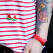 Przypinka do ubrań imitująca kawałek arbuza z pestkami. Pins w złotym wykończeniu ręcznie malowany od producenta metalowych przypinek i breloków od pinswear. Dwie przypinki wpięte w koszulkę w biało czerwone paski.
